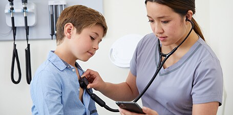 Klinický lékař auskultuje hrudník chlapce a sleduje aplikaci v telefonu
