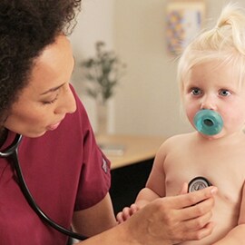 Dětská sestra provádějící poslech hrudníku batolete pomocí fonendoskopu 3M Littmann Classic III.
