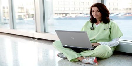 Lékař sedí na podlaze a čte si v laptopu
